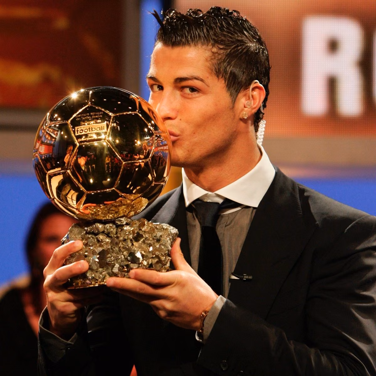 Koyu renk takım elbiseli bir adam, altın renkli Ballon d'Or ödülündeki topa dudaklarıyla dokunuyor.