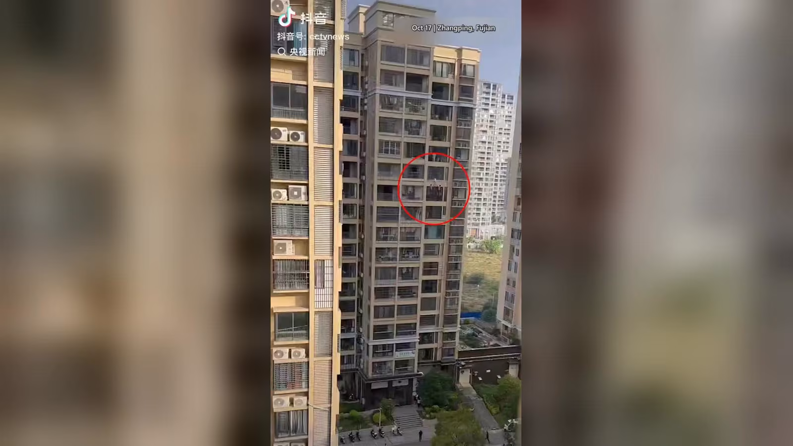 Bej renkli yüksek bir apartmanın üst katlarında, kırmızı daireyle işaretlenmiş bir pencerede küçük bir figür.
