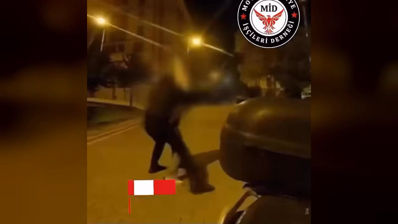 Gece bir sokakta, koyu renk kıyafetli bir kişi motosikletin siyah kutusuna doğru eğilmiş; yüzü bulanıklaştırılmış.