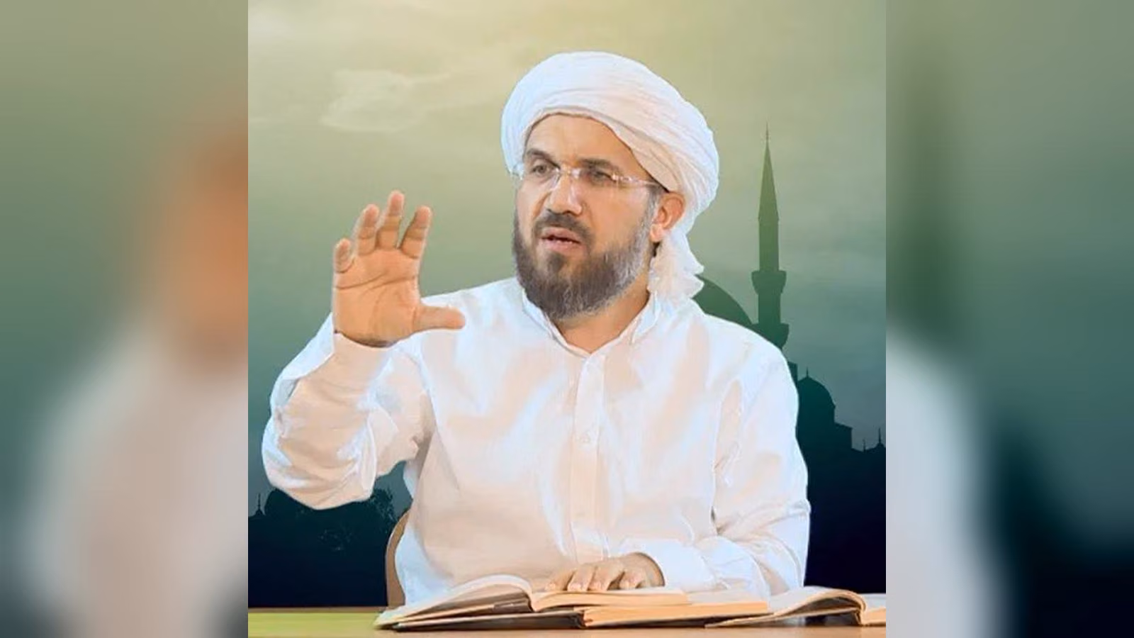 Beyaz sarıklı, gözlüklü, sakallı bir adam elini kaldırmış konuşuyor; önünde açık kitaplar, arkada cami silueti.