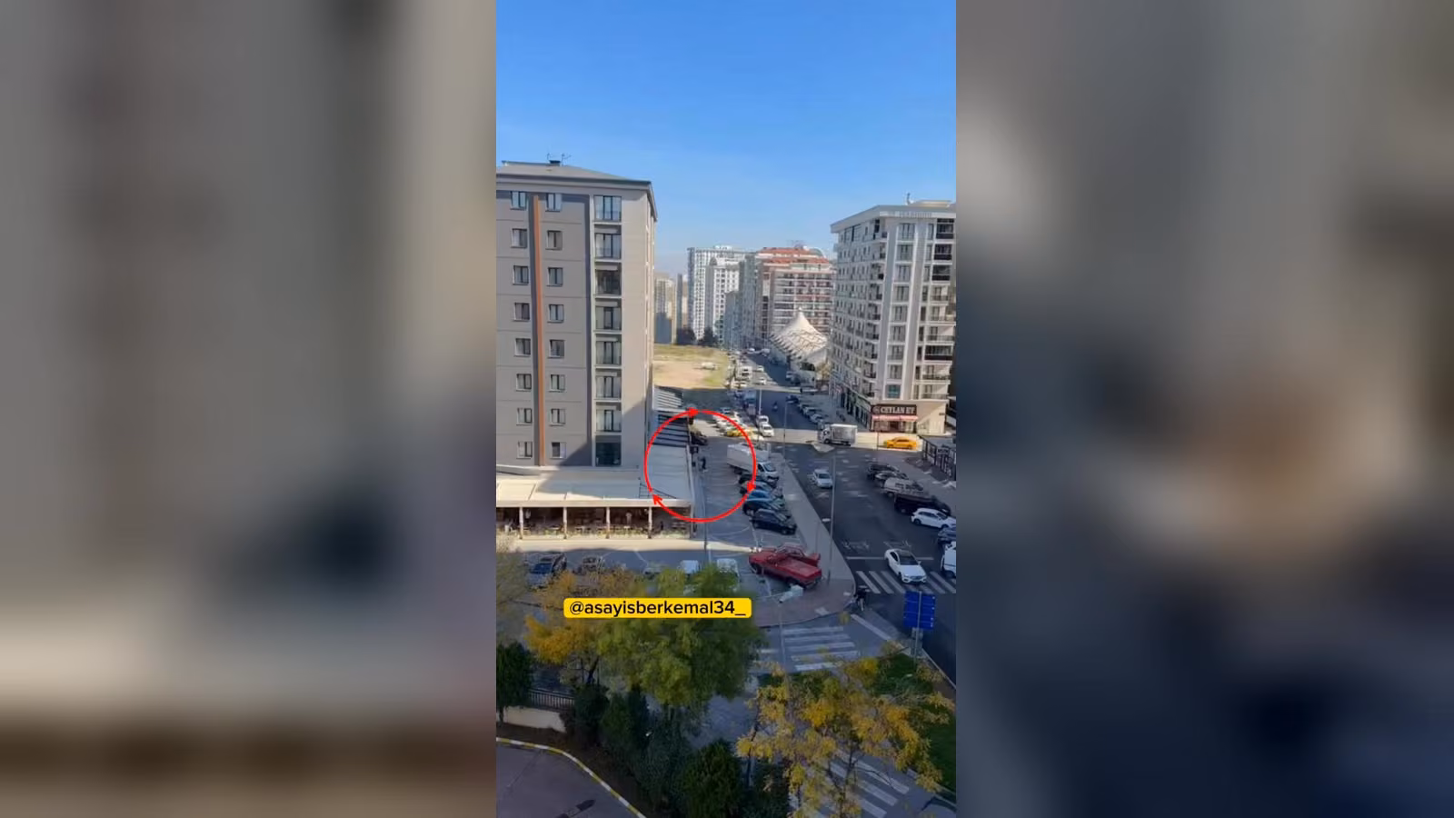 Çok katlı binaların arasındaki caddede, kırmızı daireyle işaretli köşede araçlar ve beyaz bir kamyonet var.