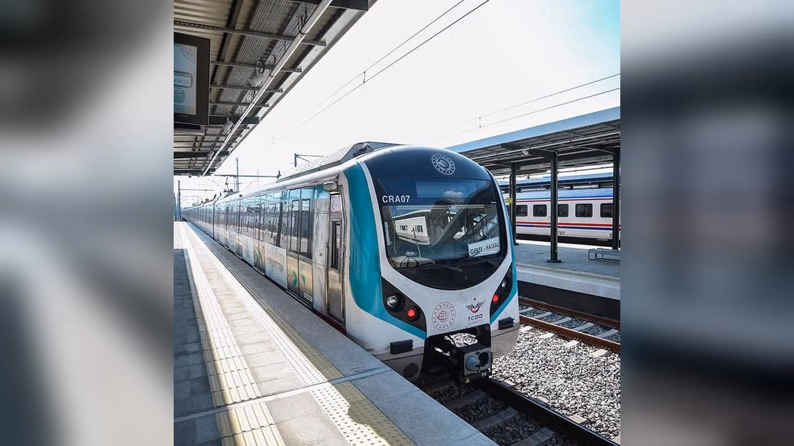 Peronda duran beyaz ve turkuaz renkli CRA07 numaralı banliyö treni; ön camındaki tabelada GEBZE - HALKALI yazıyor.