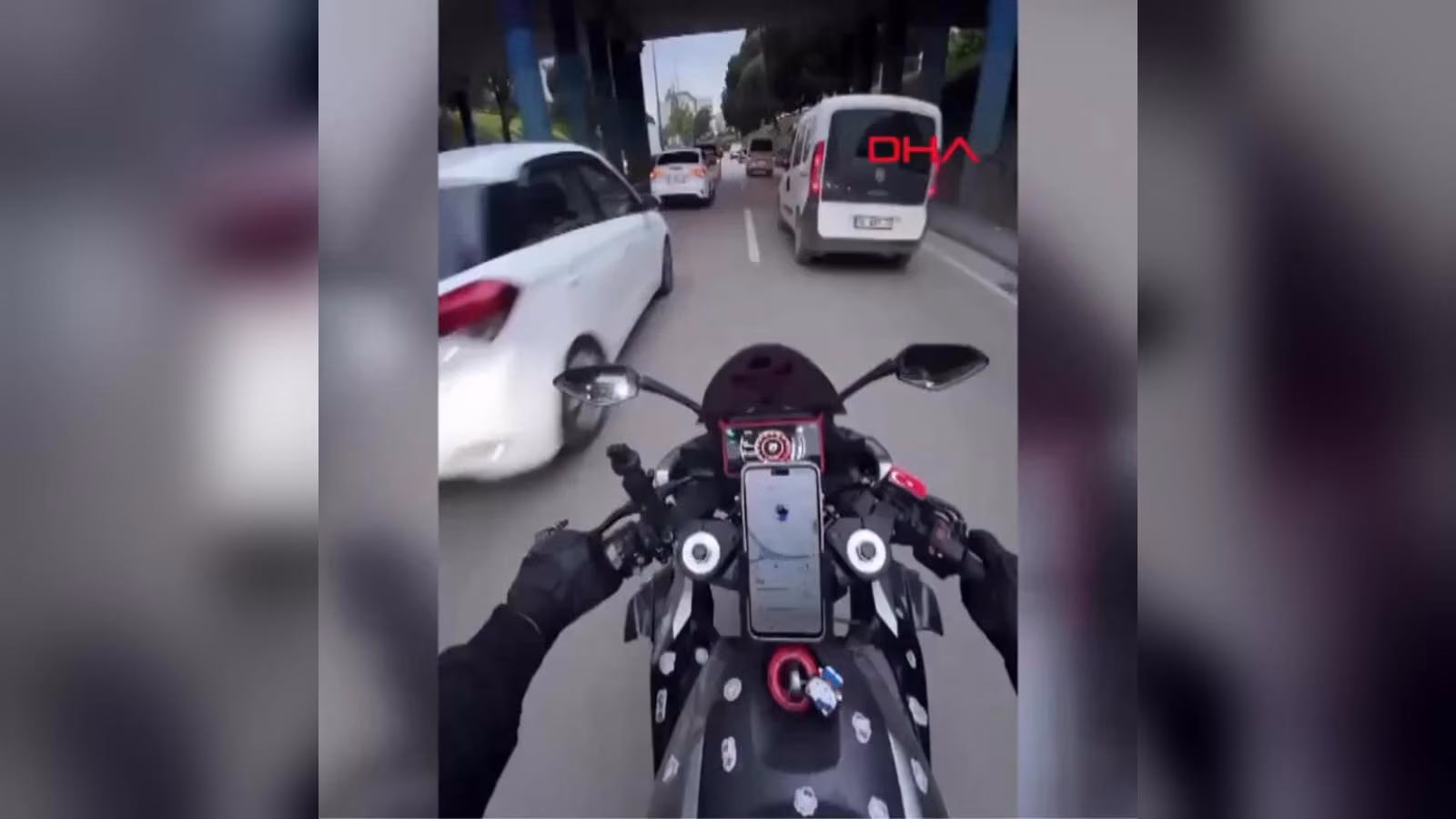 Motosiklet sürücüsünün gözünden: alt geçit altında ilerleyen trafikte beyaz otomobil ve beyaz hafif ticari araç.