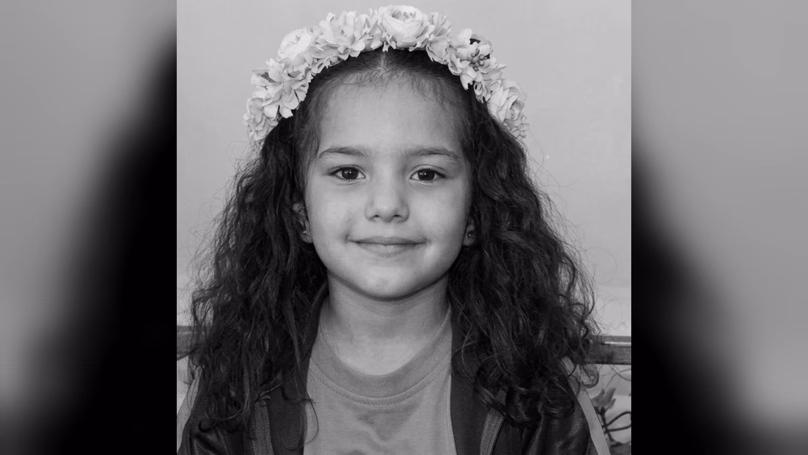 Çiçek taçlı, uzun ve kıvırcık saçlı, gülümseyen küçük bir kız çocuğunun siyah beyaz portresi.