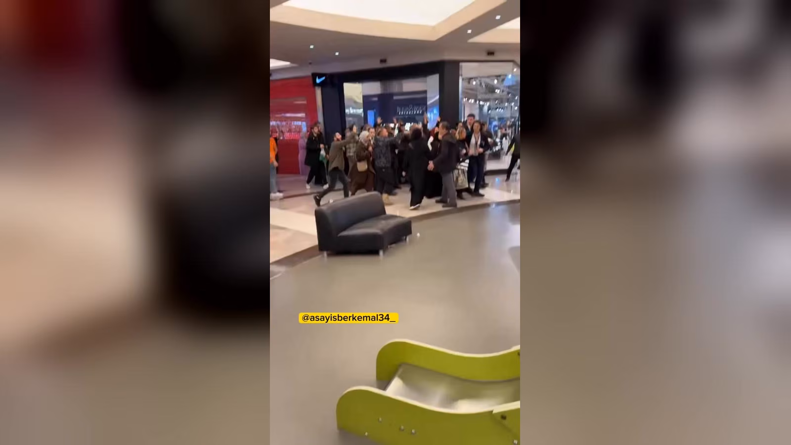 Alışveriş merkezinde Nike mağazasının önünde kalabalık bir grup yürüyor, bazı kişiler kollarını havaya kaldırmış.