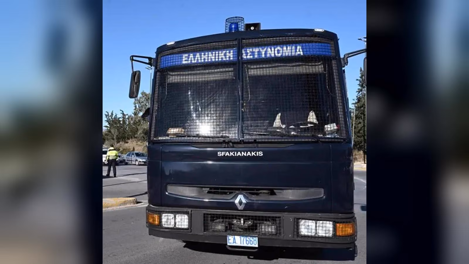 Ön camı tel örgülü, üzerinde 'Ελληνική Αστυνομία' yazan koyu mavi Yunan polis aracının önden görünümü.
